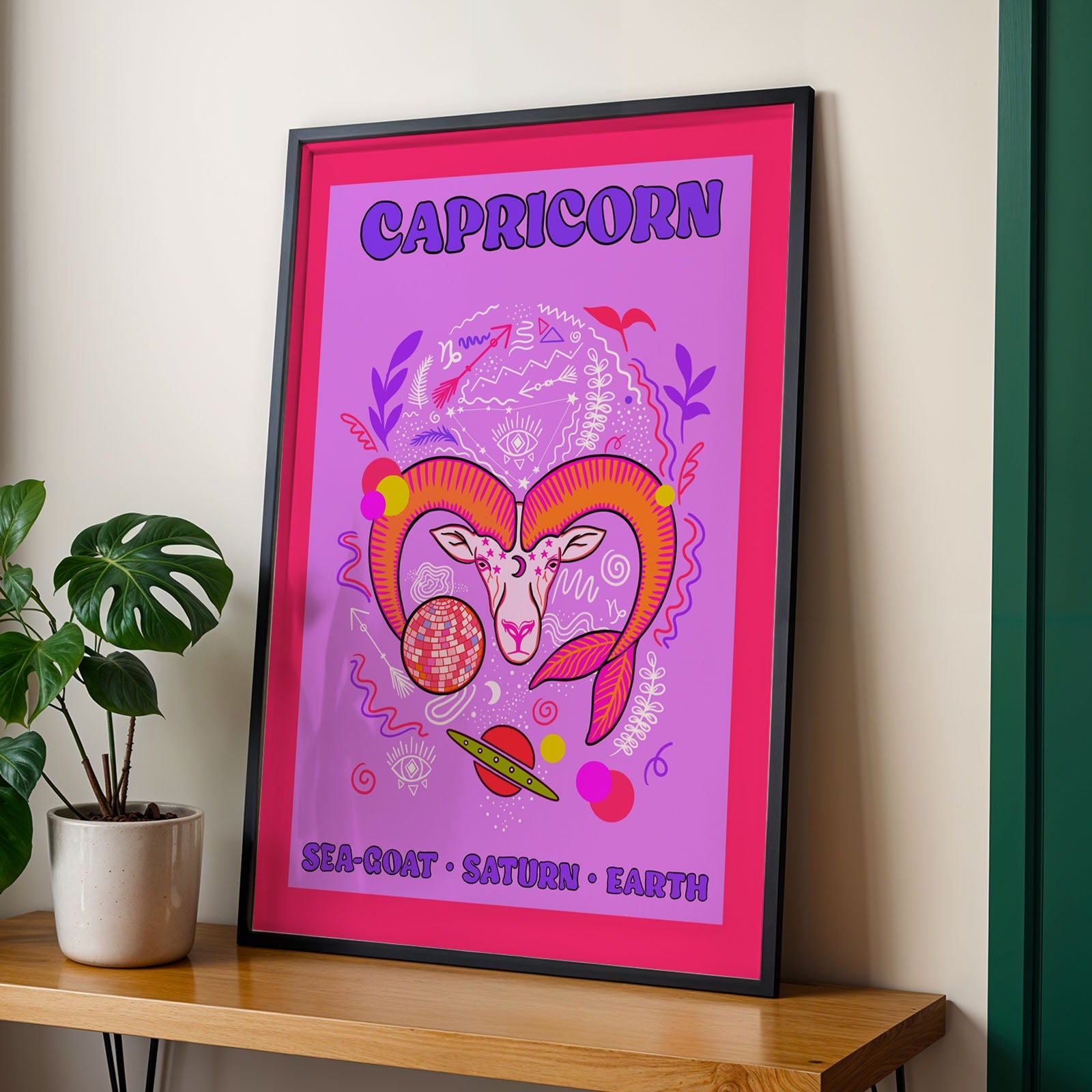 Framed poster of Capricorn design on a wall next to a plant