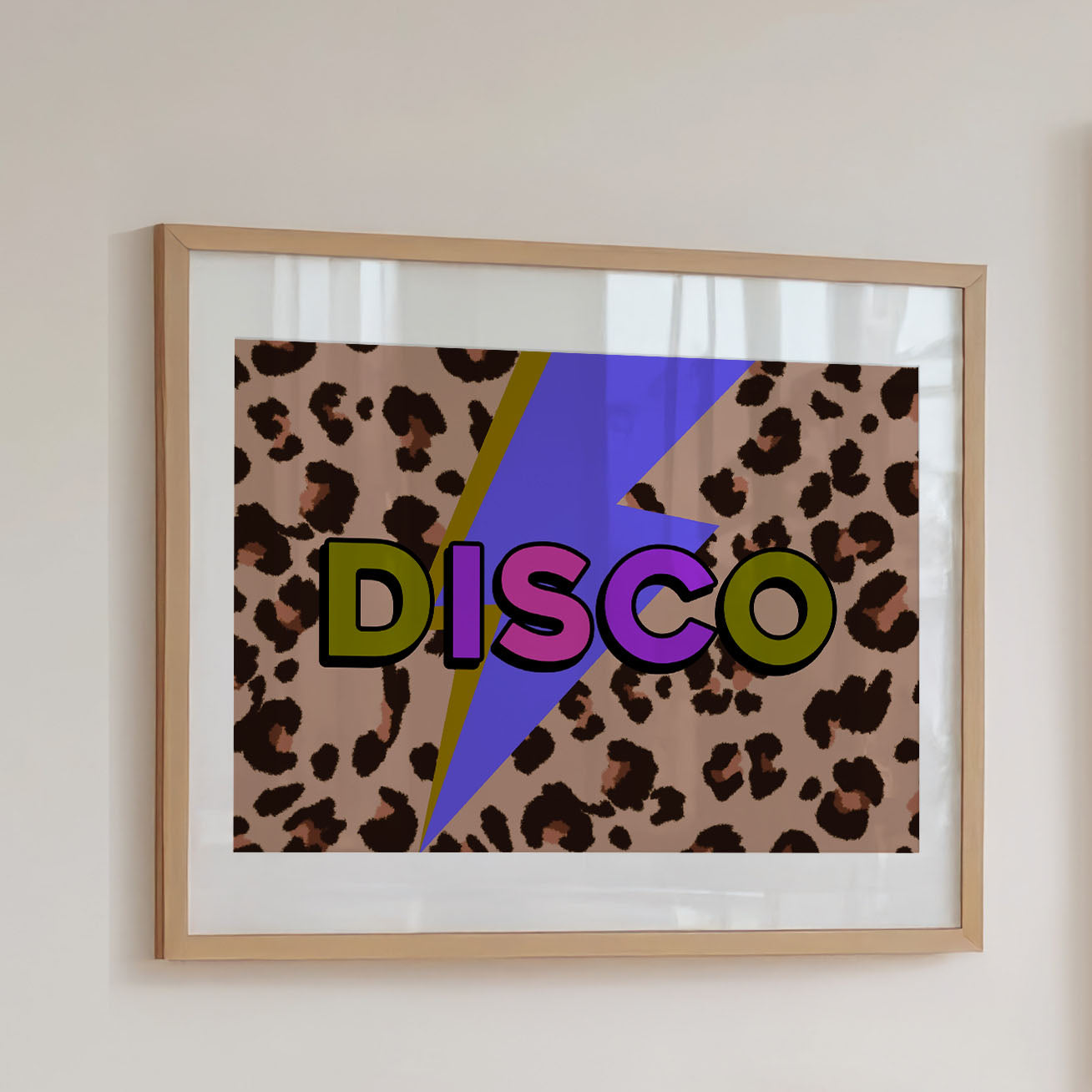 A framed art print featuring a retro 1970s-style 'DISCO' graphic with bold multicolored letters over a leopard print background and a purple lightning bolt, hung on a light beige wall.