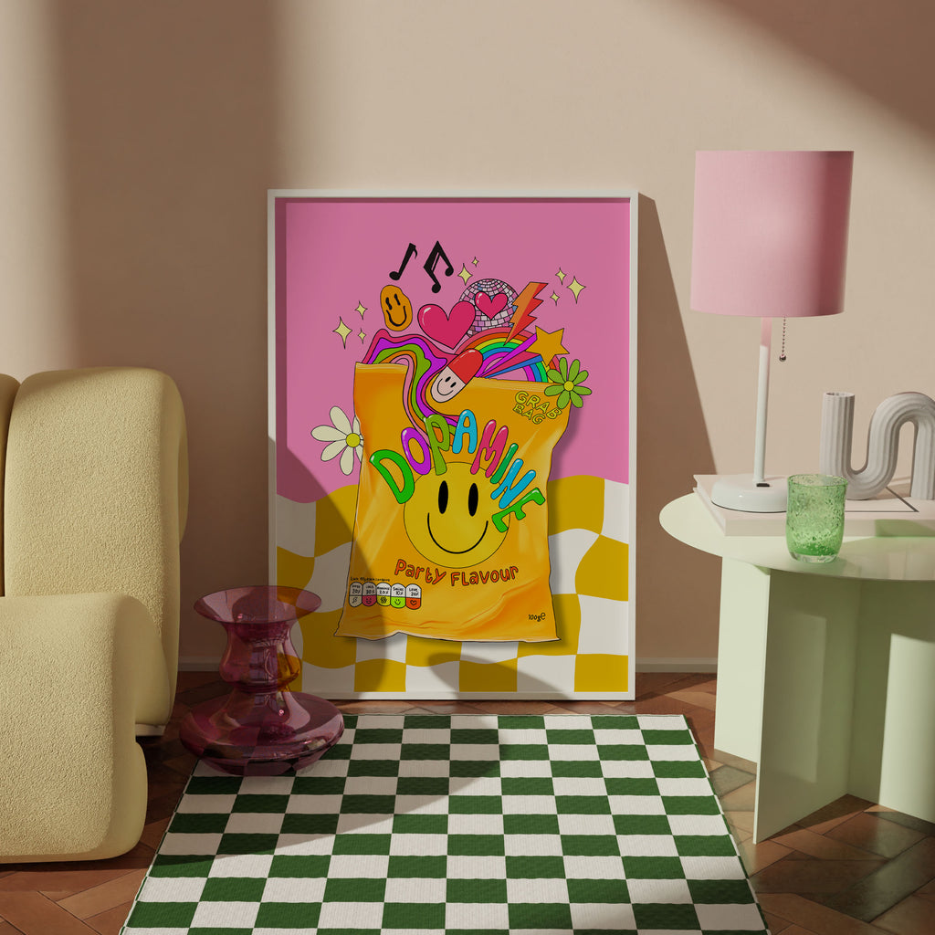 A framed colorful poster leaning against a beige wall in a styled room. The art print features a bright pink background, a yellow smiley-face bag labeled 'DOPAMINE Party Flavour,' and playful multicolor doodles.