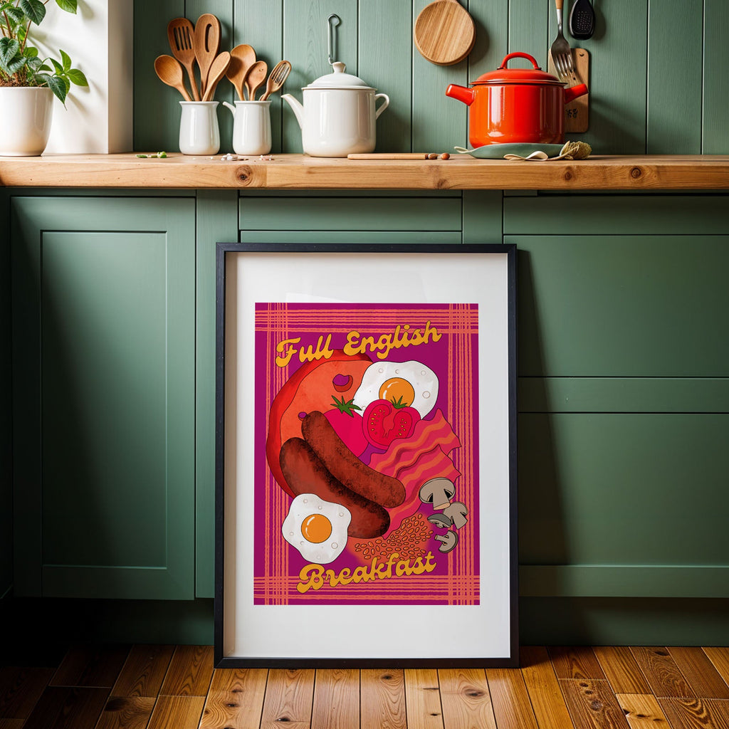 A framed art print featuring a colorful breakfast illustration with the text 'Full English Breakfast' leans against a green kitchen cabinet on a wooden floor.