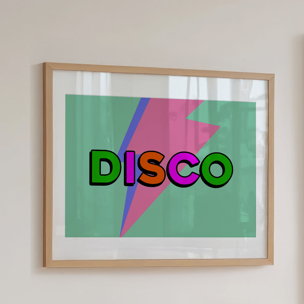 Framed wall art hanging on a light beige wall, featuring the word "DISCO" in bold retro letters over a mint green background with a pink and blue lightning bolt graphic.