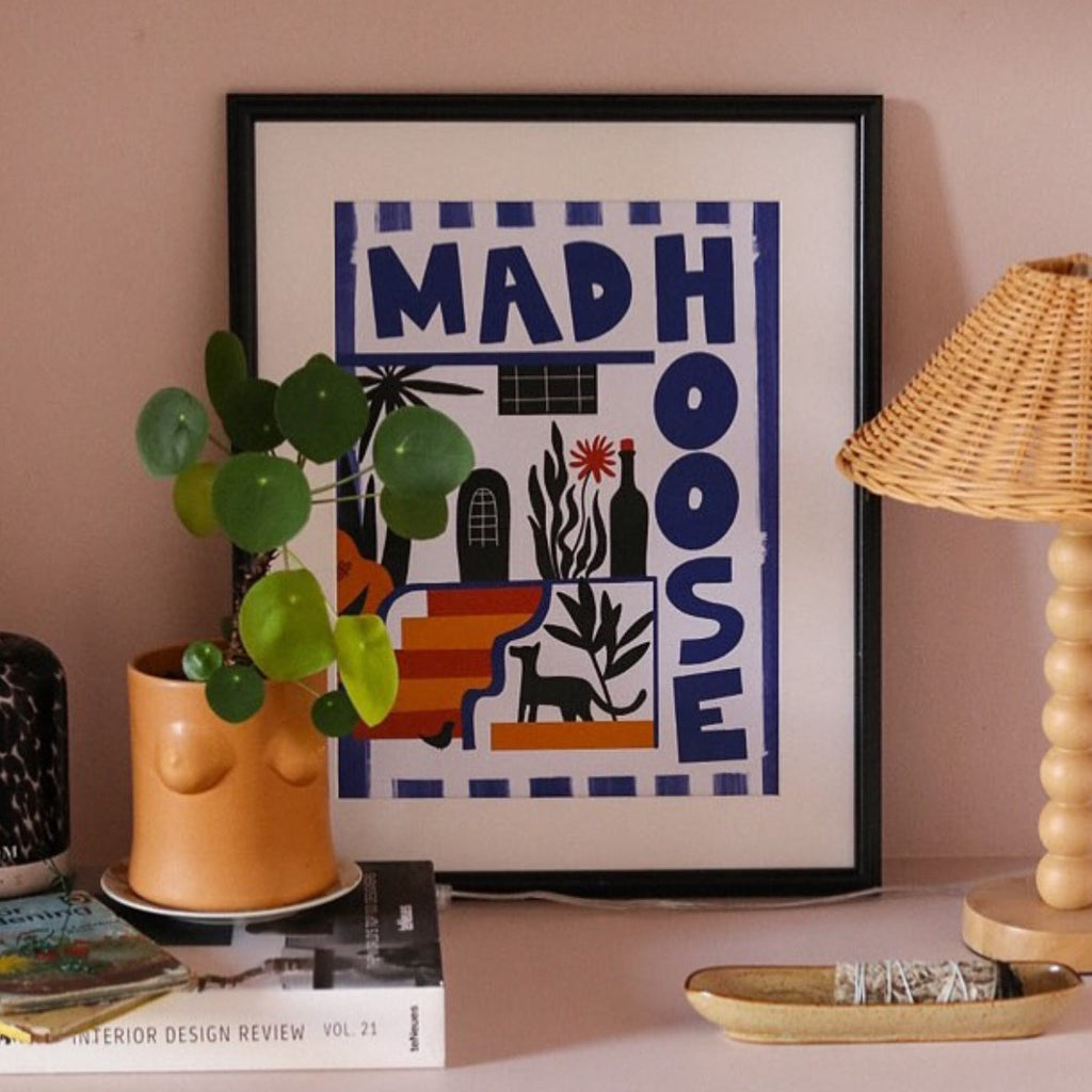 Framed artwork with 'MADHOUSE' design on a shelf with decor items.