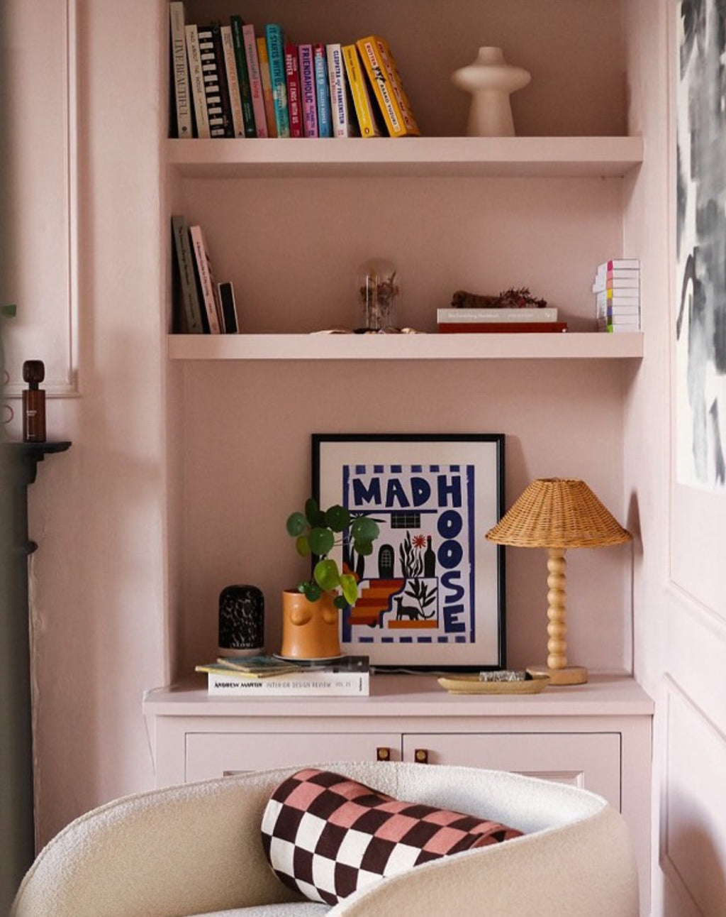 Nook with a bookshelf, lamp, and framed picture on a pink wall.